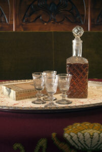 Pöydän päällä tarjottimella lasinen konjakkipullo pyöreällä korkilla, neljä lasia sekä sikarilaatikko.