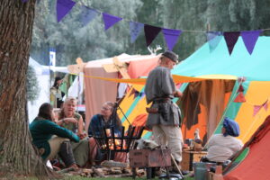 Keskiaikamarkkinoiden osallistujia ja värikkäitä telttoja. Ihmisillä yllään keskiajan tyylisiä vaatteita.