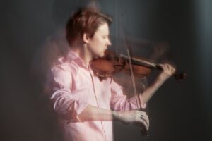 Mies vaaleanpunaisessa kauluspaidassa soittaa viulua.