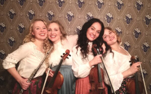 Neljä hymyilevää nuorta naista. Kolmella kädessä viulu, yhdellä poikkihuilu.