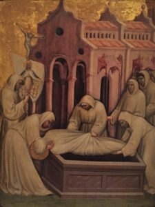 Kuusi hupullisiin kaapuihin pukeutunutta henkilöä laskee kankaaseen käärittyä ruumista arkkuun. Taustalla kirkko. Valokuva maalauksesta.