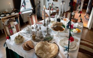 Palanderin talon ruokasalin pöytä, johon on katettu jouluruokia. Joulukoristeköynnökset roikkuvat katosta pöydän yläpuolella.