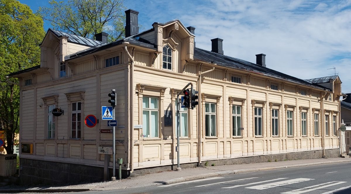 Palanderin talon julkisivu. Suuri, vaalea, yksikerroksinen puurakennus.