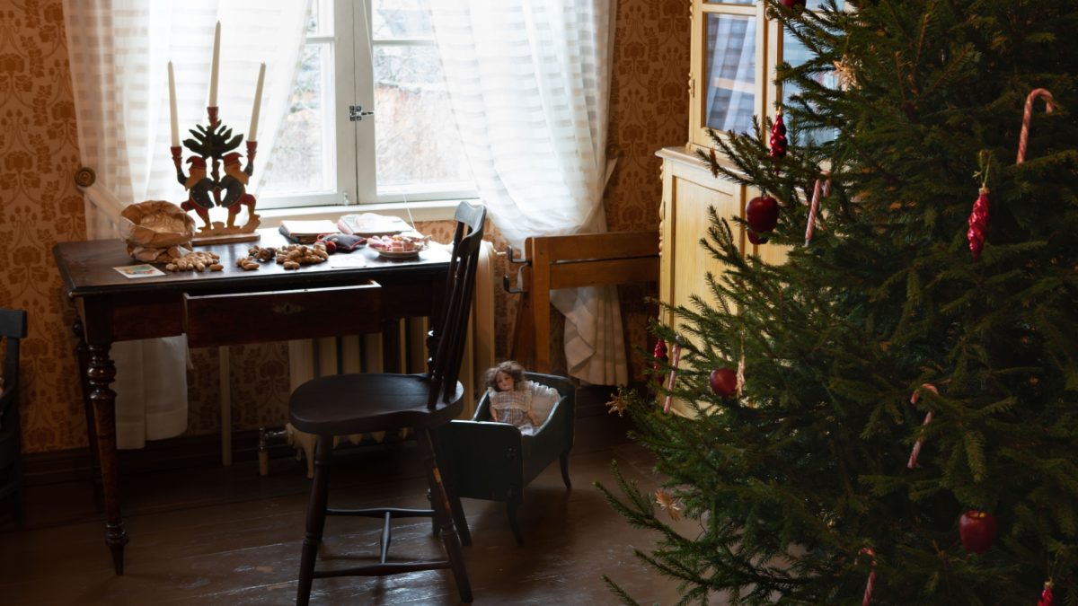 Oikeassa laidassa etualalla koristeltu joulukuusi. Taaempana ikkunan edessä kirjoituspöytä, jonka päällä on kolmihaarainen kynttelikkö ja pähkinöitä.