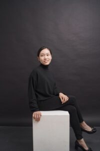 Pianisti Myra Pranajaya istuu valkoisen kuutiomaisen istuimen päällä mustissa vaatteissa