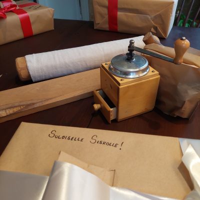 Lähikuvassa joulupaketti, jossa lukee "Suloiselle siskolle", kahvimylly ja kaulauslauta.