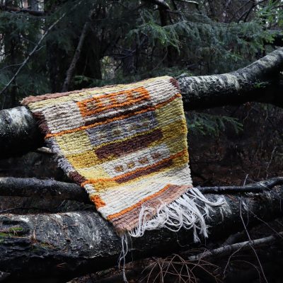 Värikäs ryijy roikkuu metsässä koivunrungolla.